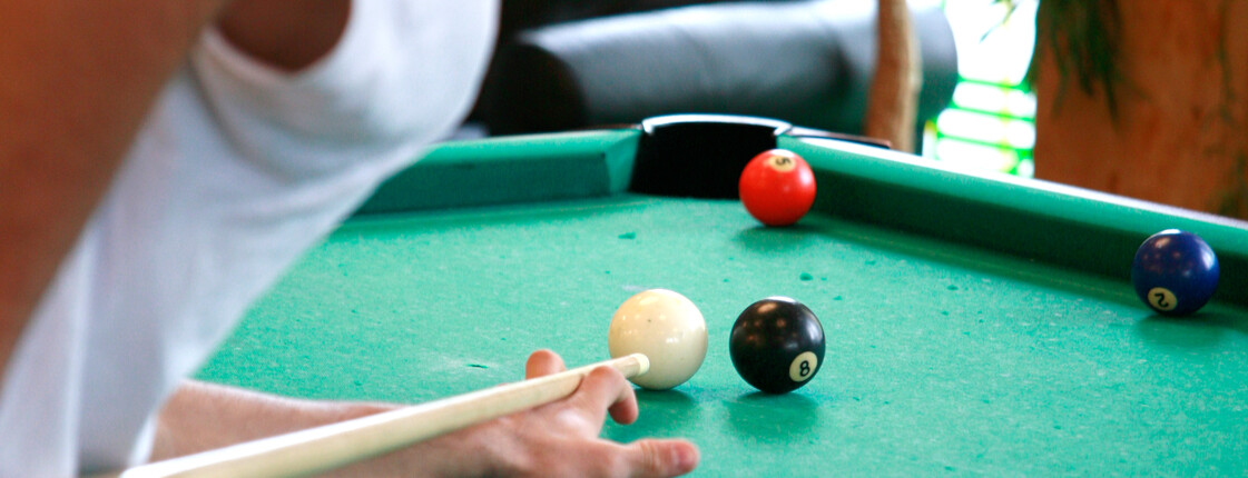 Billard im JuZe Space Eine Jugendlicher mit weißen T-Shirt und Cap beim Billard spielen.