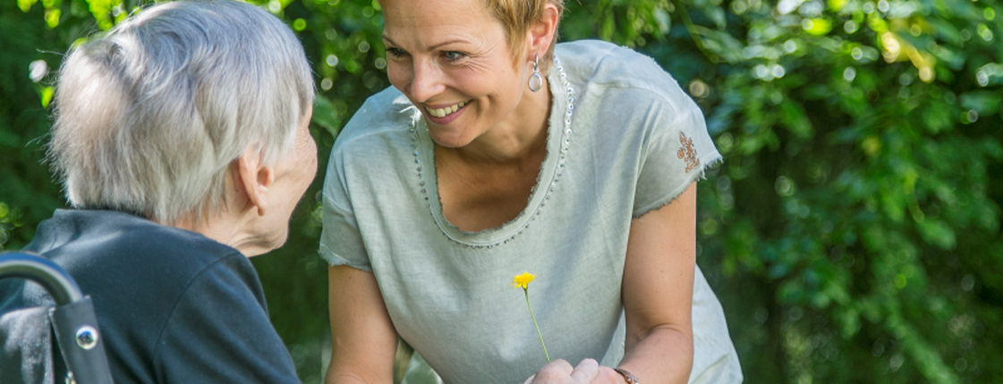 Eine Frau spricht mit einer im Rollstuhl sitzenden Seniorin