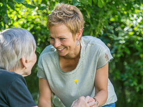 Eine Frau spricht mit einer im Rollstuhl sitzenden Seniorin