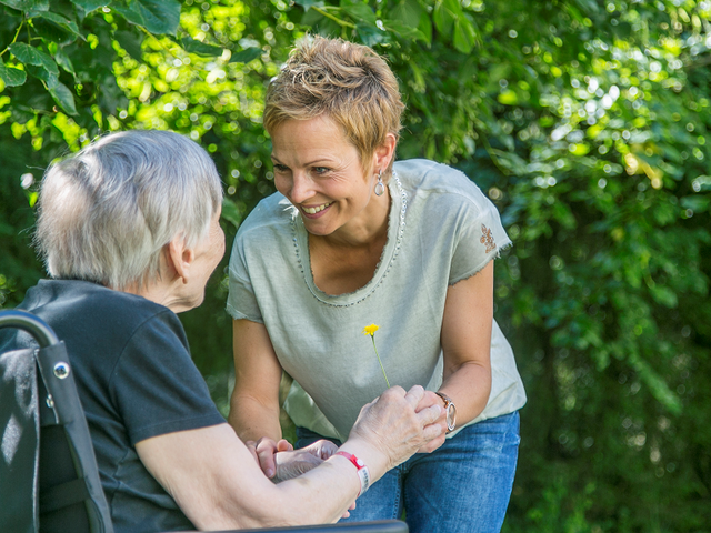 Eine Frau spricht mit einer im Rollstuhl sitzenden Seniorin