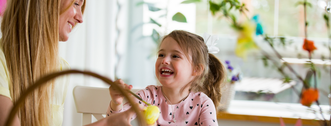 Ein Kind bemalt ein Osterei und lacht