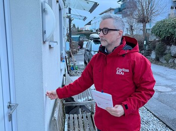 Ein Mann mit Caritas Jacke läutet an einer Haustür