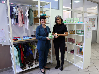 Zwei Frauen stehen in einem großen, hellen raum vor zwei weißen Regalen mit Sachspenden.