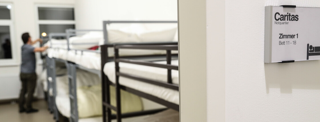 Ein Mann steht an einem Stockbett und schüttelt den Kopfpolster auf.
