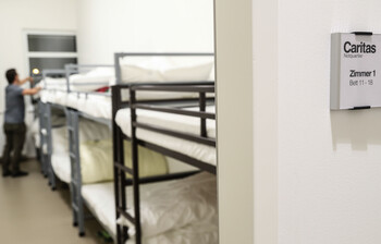 Ein Mann steht an einem Stockbett und schüttelt den Kopfpolster auf.