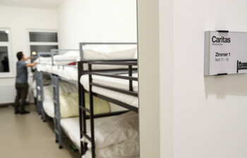 Ein Mann steht an einem Stockbett und schüttelt den Kopfpolster auf.