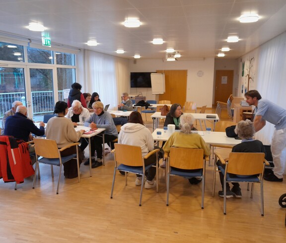 Ältere Menschen sitzen mit Computer und Smartphone an Tischen