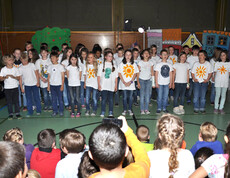 Kinder performen vor Kindern in einem Turnsaal. Die Performer haben alle ein weißes T-Shirt an. 