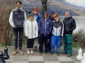 Eine Gruppe von Menschen mit Beeinträchtigung stehen vor einem See und blicken in die Kamera.