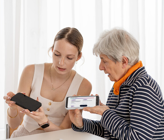 Eine junge Frau erklärt einer Seniorin das Smartphone