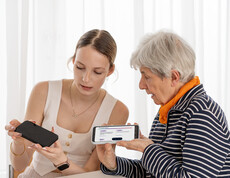 Eine junge Frau erklärt einer Seniorin das Smartphone