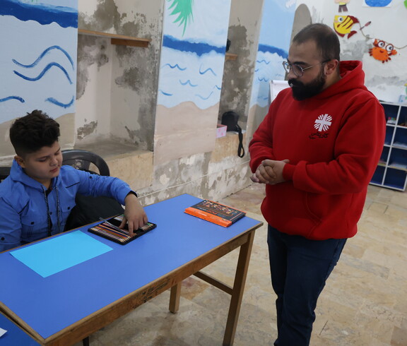 Ein Junge wird von einem Caritas Mitarbeiter in Syrien unterrichtet