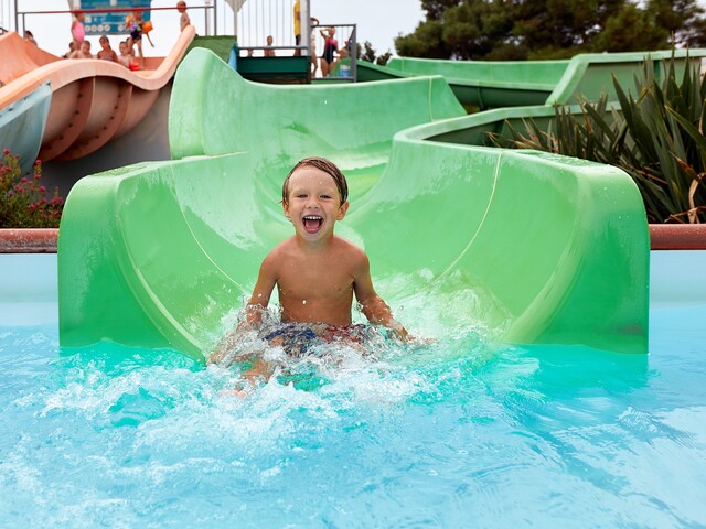 Ein Kind rutscht eine Wasserrutsche ins Schwimmbad hinunter