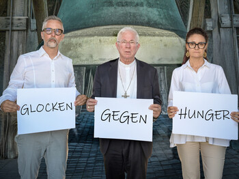 3 Personen halten ein Schild mit dem Text "Glocken gegen Hunger"