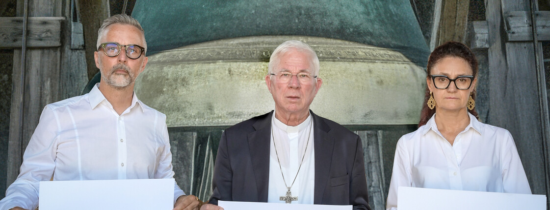 3 Personen halten ein Schild mit dem Text "Glocken gegen Hunger"
