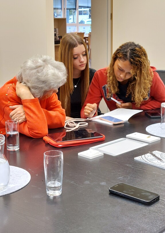 Zwei Jugendliche und eine Seniorin schauen aufs Smartphone