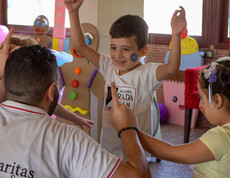 Zwei Kinder spielen mit einem Caritas Syrien Mitarbeiter