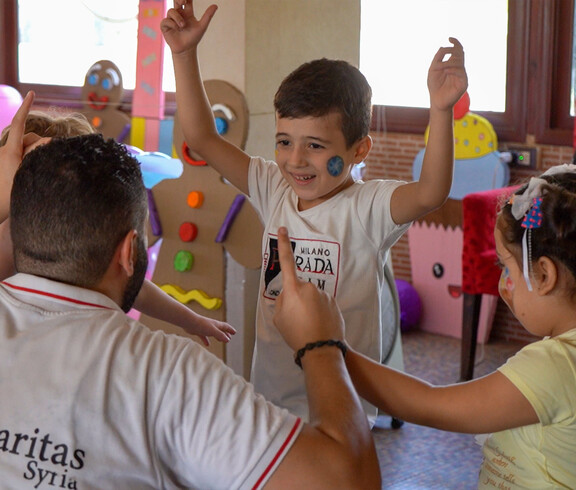 Zwei Kinder spielen mit einem Caritas Syrien Mitarbeiter