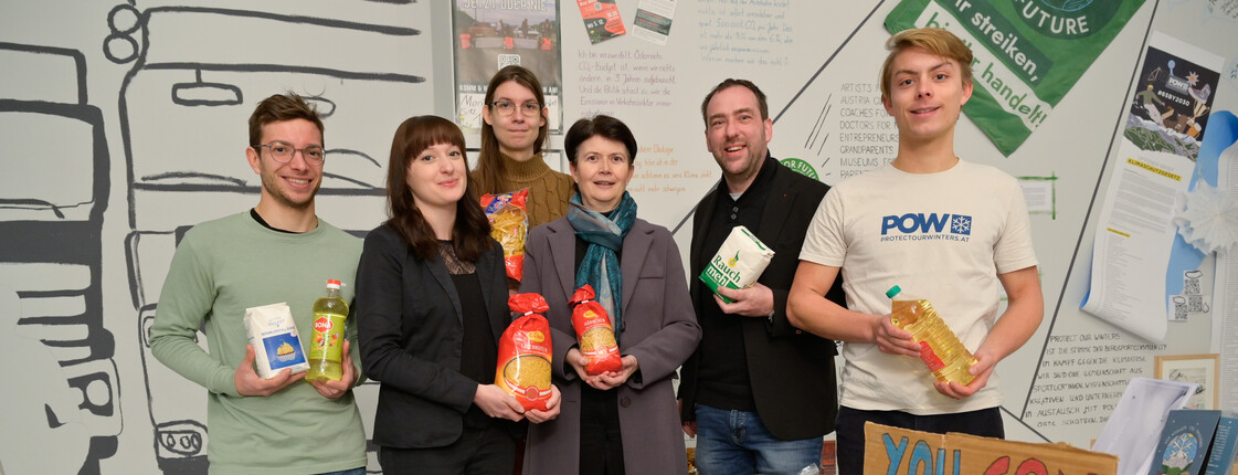 Sechs Personen stehen hinter Kisten voll Lebensmitteln zu einem Gruppenfoto zusammen.