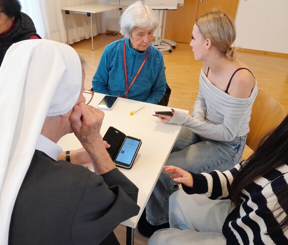 Eine Schülerin erklärt einer Nonne und einer älteren Frau das Smartphone