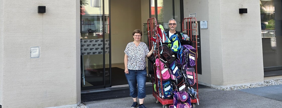 Eine Frau und ein Mann mit einem Berg aus Schultaschen