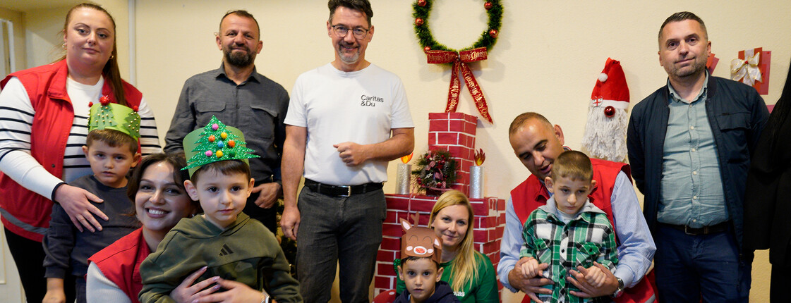 Gruppe von Erwachsenen und Kindern bei einer weihnachtlichen Hilfsaktion mit Deko, Geschenken und Nikolausfigur.