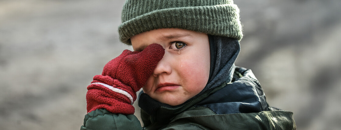 Kind mit Mütze und roten Handschuhen wischt sich weinend die Augen ab