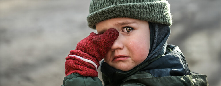 Kind mit Mütze und roten Handschuhen wischt sich weinend die Augen ab