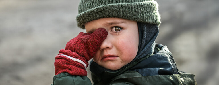 Kind mit Mütze und roten Handschuhen wischt sich weinend die Augen ab