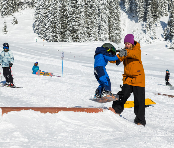 Ein Kind lernt Snowboarden mit einer Trainerin