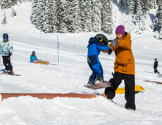 Ein Kind lernt Snowboarden mit einer Trainerin