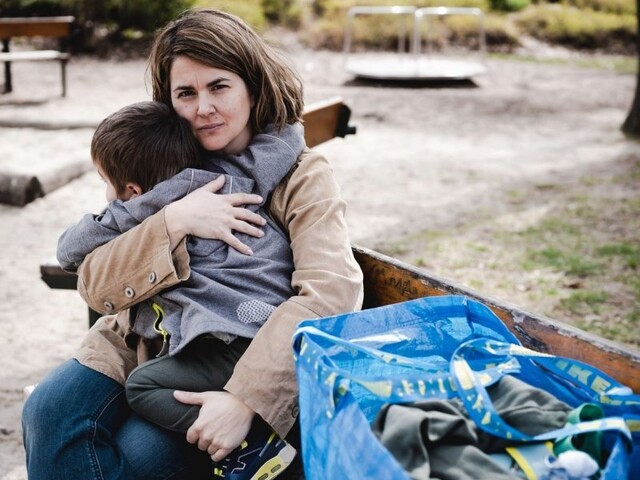 Eine Frau sitzt mit ihrem Kind und einem Sack voll Habseligkeiten auf einer Parkbank..