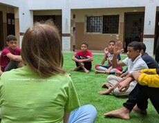 Eine Gruppe Kinder und eine Betreuerin sitzen auf einem Fußballrasen