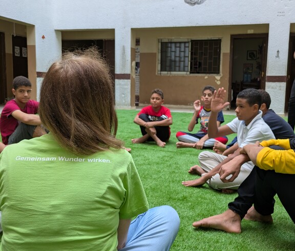 Eine Gruppe Kinder und eine Betreuerin sitzen auf einem Fußballrasen