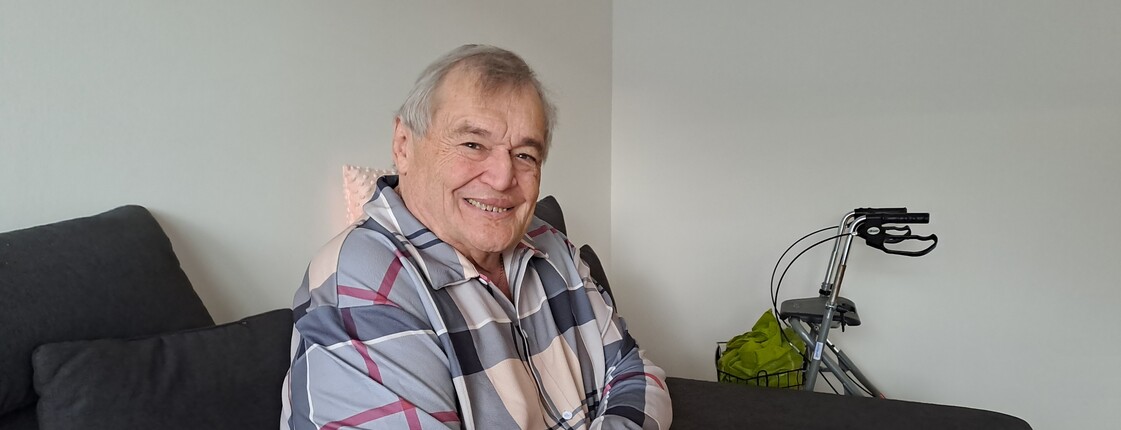 Ein älterer Mann mit Rollator sitzt auf einem Sofa