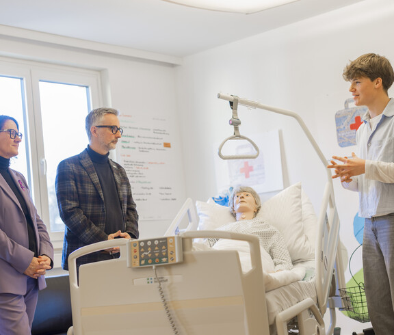 Ein Schüler und zwei Erwachsene vor einer Pflegepuppe