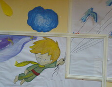 An einer gelben Wand hängen bemalte Papierblätter, die ein Gesamtbild ergeben, das den Kleinen Prinzen zeigt.