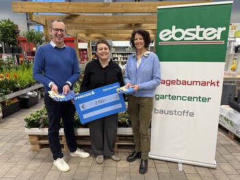 Drei Personen stehen mit einem Spendenscheck in einem Baumarkt