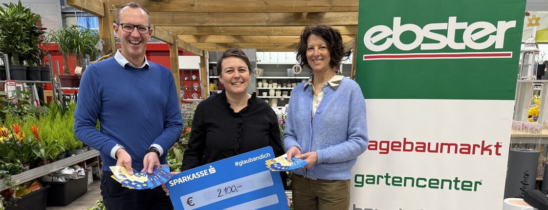 Drei Personen stehen mit einem Spendenscheck in einem Baumarkt