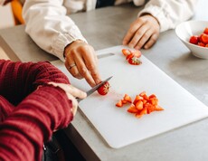 Eine Caritas Mitarbeiterin und eine Klientin schneiden Erdbeeren