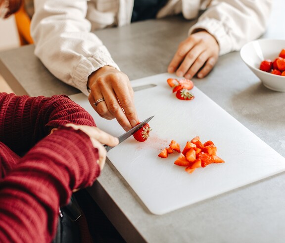 Eine Caritas Mitarbeiterin und eine Klientin schneiden Erdbeeren