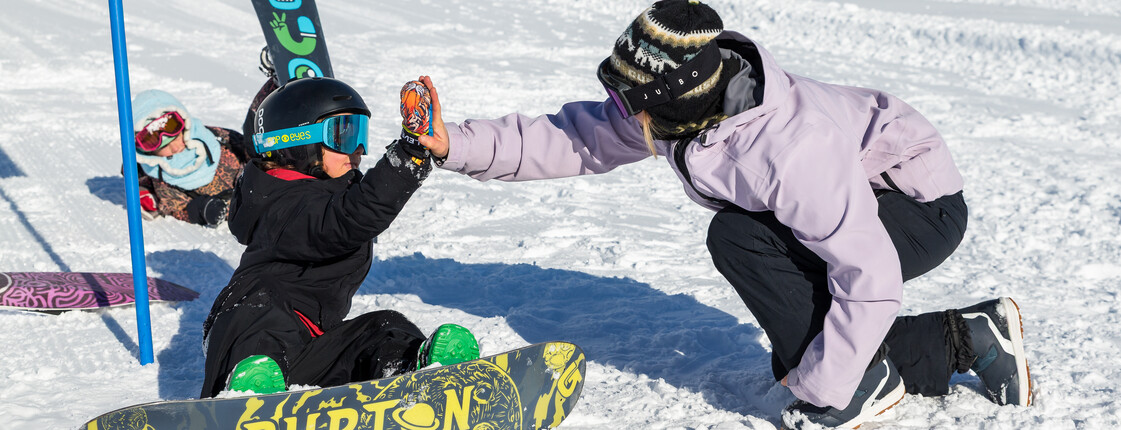 Ein Kind und eine Trainerin beim Snowboardlernen