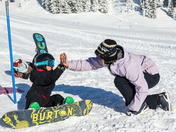 Ein Kind und eine Trainerin beim Snowboardlernen