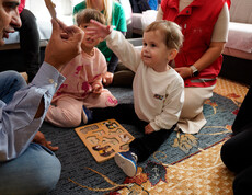 Kind hebt ein Puzzleteil hoch, während andere Teile auf dem Teppich liegen