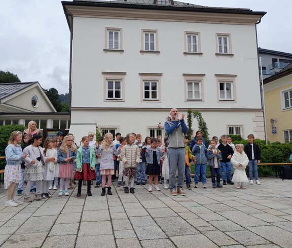 Eine Gruppe Kinder singt im Chor vor der Schule