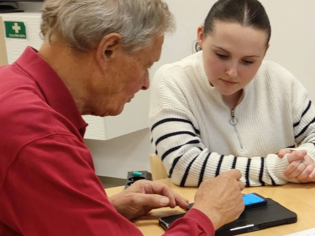 Eine junge Frau erklärt einem älteren Mann ein Smartphone