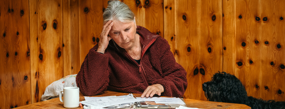 Eine Frau sitzt an einem Tisch und sieht nachdenklich auf Rechnungen