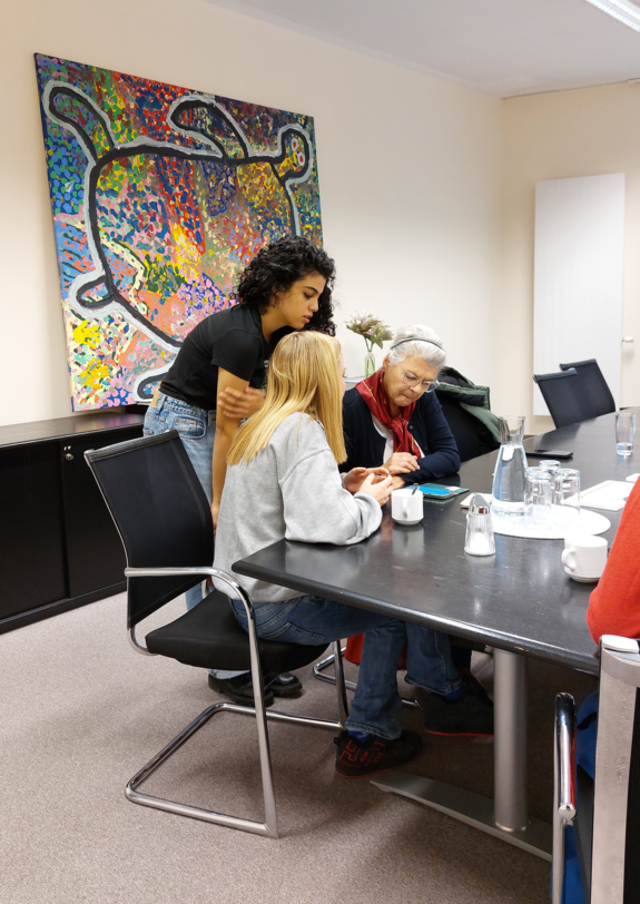 Zwei Schülerinnen und eine Seniorin schauen aufs Smartphone