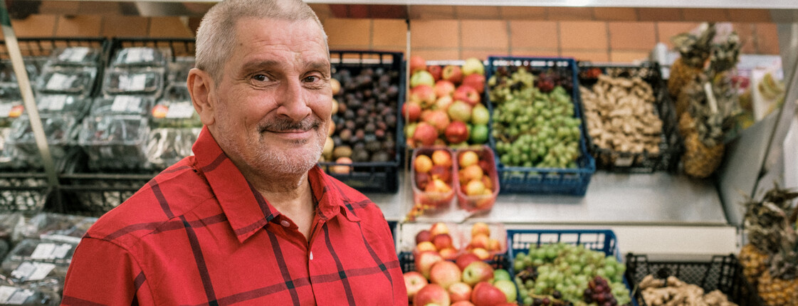 Mann in Lebensmittelausgabestelle Mann blickt zur Kamera, im Hintergrund ein Obst- und Gemüseregal