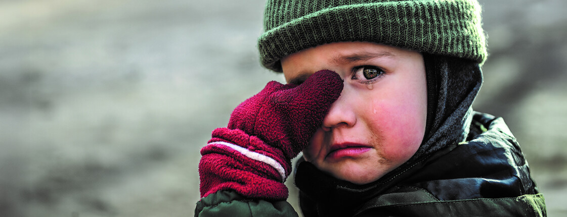 Ein weinendes Kind mit Mütze und roten Handschuhen wischt sich eine Träne aus dem Augenwinkel.